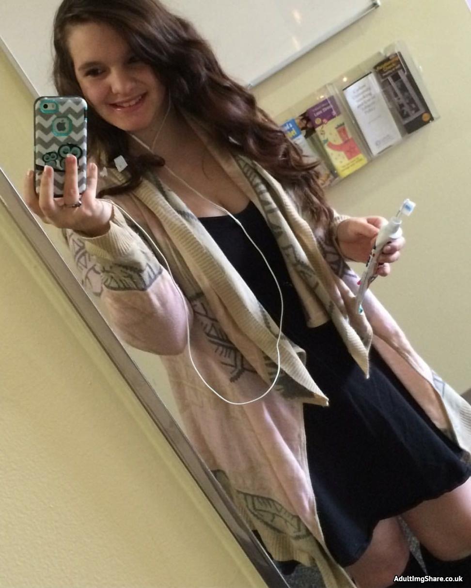 A super cute teen in a black dress takes a mirror selfie